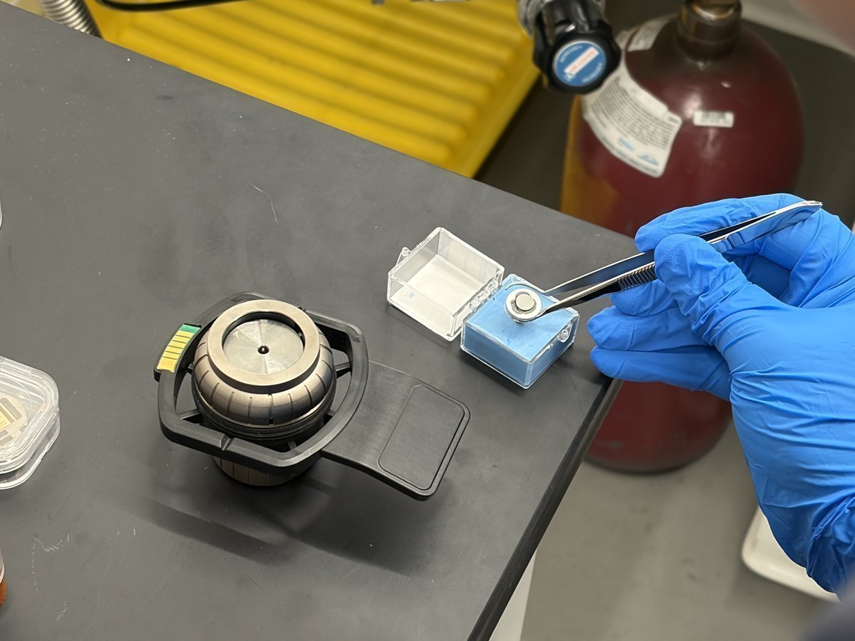 Tweezers reaching into the orange-capped storage tube to retrieve the new sample